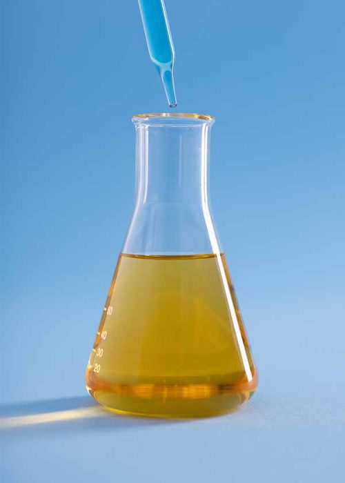 A vertical closeup of a dropper with blue liquid over an Erlenmeyer flask with yellow liquid on a blue background