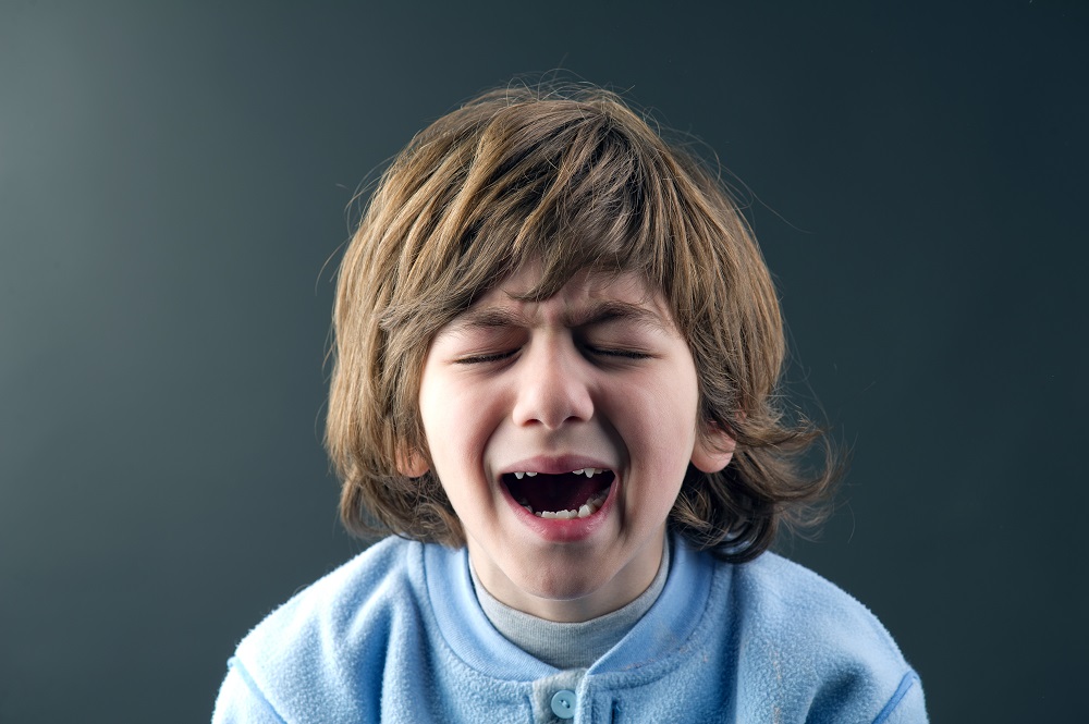 Beautiful young child crying isolated against grey background